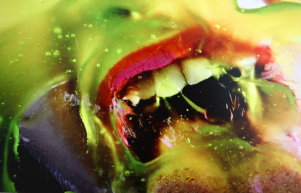 Close up image of a woman's open mouth licking at green liquid