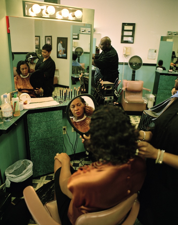 Black woman sitting in a chair at the hair salon, looking at her reflection in a hand mirror
