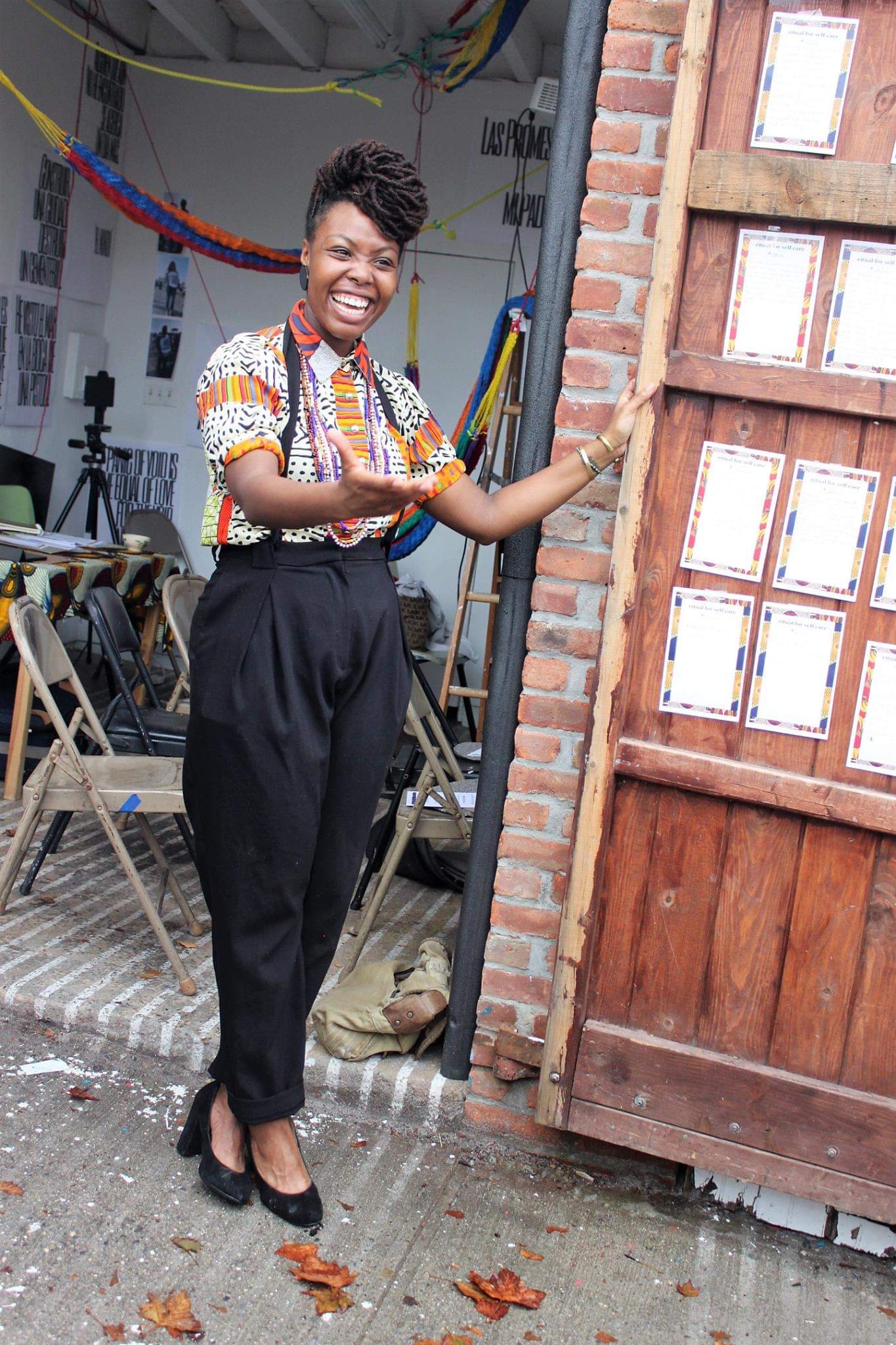 Smiling black woman standing outside near an open wood door.
