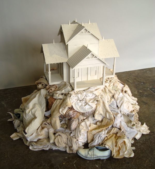 A white doll house resting a top of a pile of white clothing