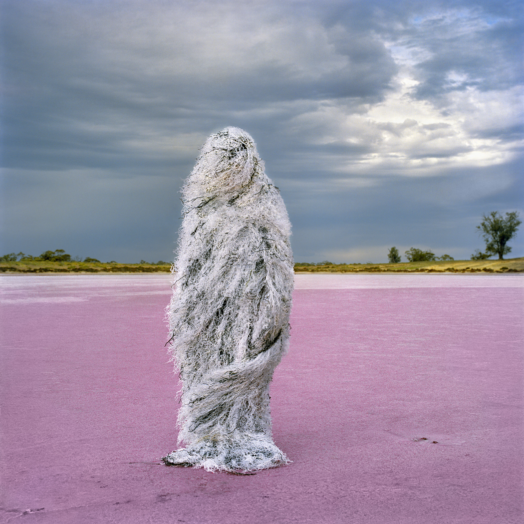 Person wearing a ghillie suit, standing in a stark landscape