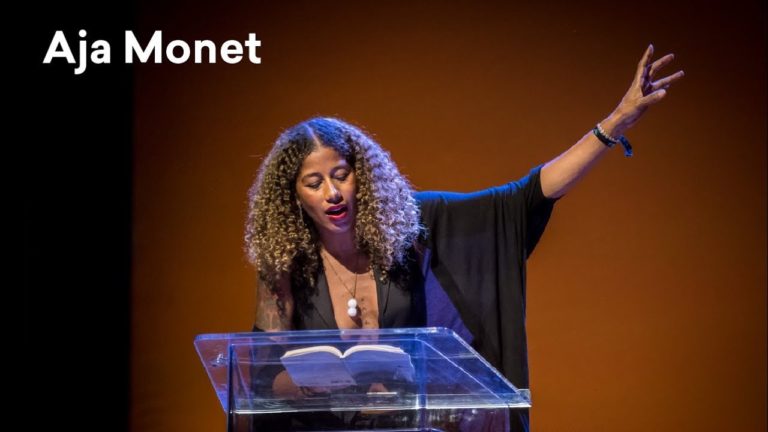 A black woman stands behind a podium, reading from a book.